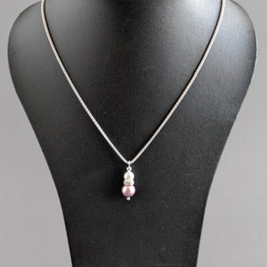 May include: A silver chain necklace with a pendant featuring a pink pearl and a white pearl with a clear crystal accent.