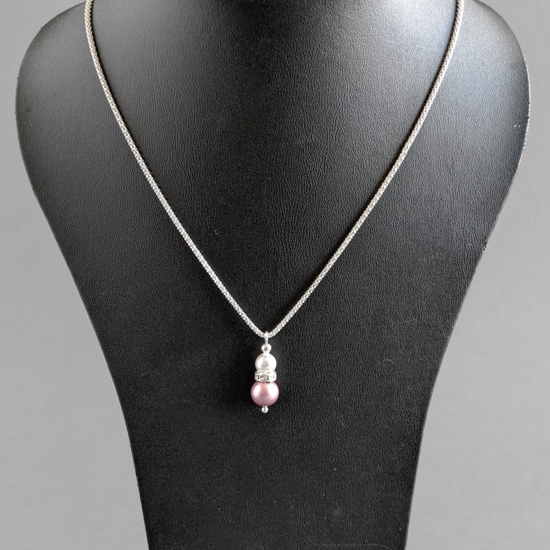 May include: A silver chain necklace with a pendant featuring a pink pearl and a white pearl with a clear crystal accent.