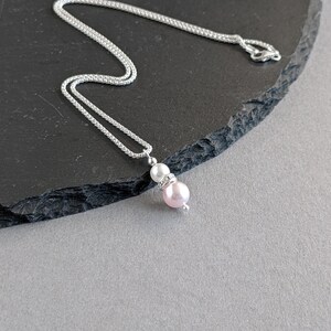 May include: A silver chain necklace with a pink and white pearl pendant. The pendant has a small rhinestone accent.