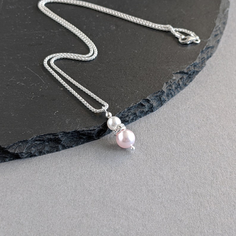 May include: A silver chain necklace with a pink and white pearl pendant. The pendant has a small rhinestone accent.
