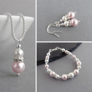 May include: A set of pink and white pearl jewelry with a necklace, bracelet, and earrings. The jewelry is made with silver chain and has a delicate design.