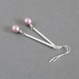 May include: A pair of silver earrings with a mauve pearl on each earring. The earrings have a long, straight silver bar and a small silver hook.