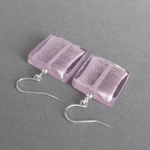 May include: A pair of silver dangle earrings with square shaped pink glass pendants. The glass has a silver foil design.