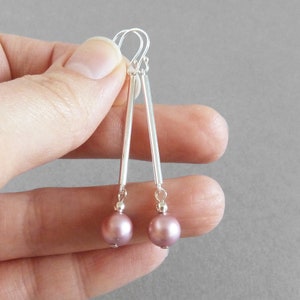 May include: Silver dangle earrings with a long, thin silver bar and a single mauve pearl at the bottom.
