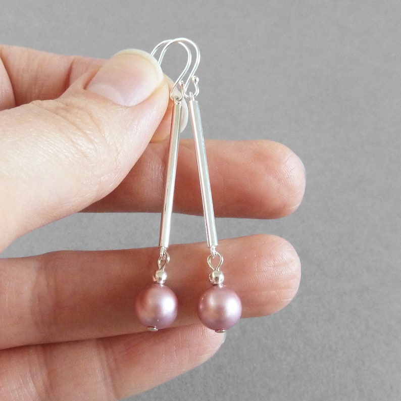 May include: Silver dangle earrings with a long, thin silver bar and a single mauve pearl at the bottom.