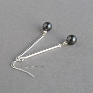 Puede incluir: Un par de pendientes de plata con cuentas negras. Los pendientes tienen una barra larga y delgada de plata con una cuenta negra en el extremo.