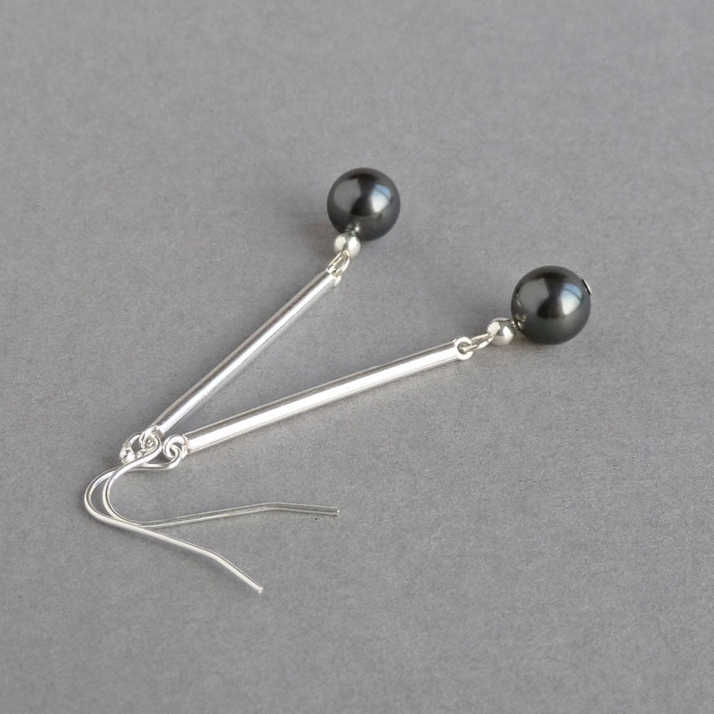 Puede incluir: Un par de pendientes de plata con cuentas negras. Los pendientes tienen una barra larga y delgada de plata con una cuenta negra en el extremo.
