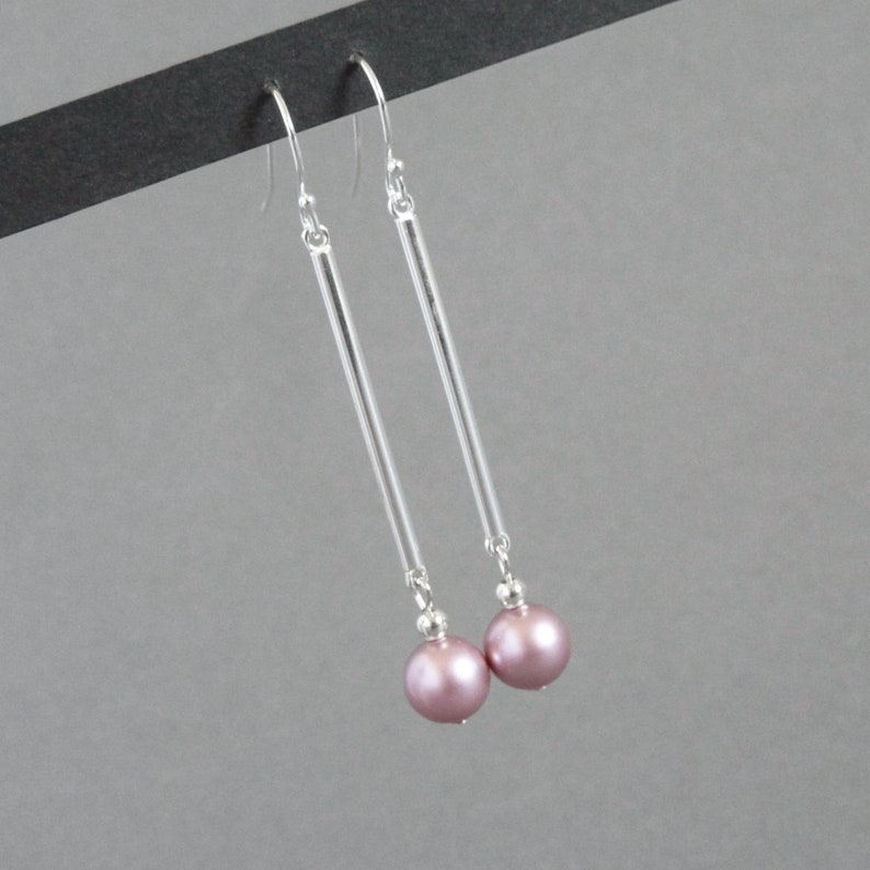 May include: A pair of silver dangle earrings with a long, thin bar and a single pink pearl at the end of each earring.