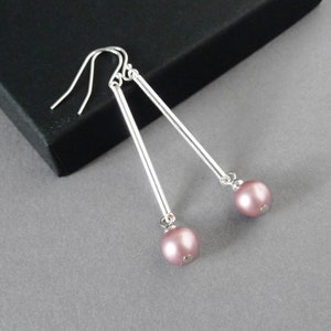 May include: A pair of silver dangle earrings with a pink pearl at the end of each earring.