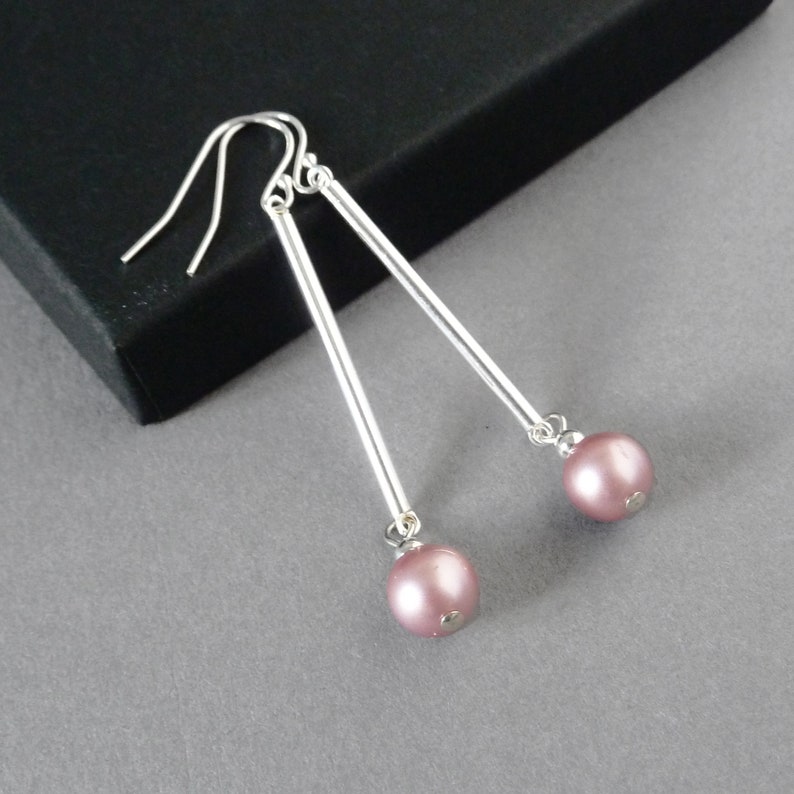 May include: A pair of silver dangle earrings with a pink pearl at the end of each earring.
