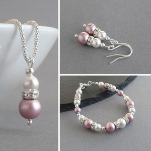 May include: A set of jewelry featuring a necklace, earrings, and a bracelet. The jewelry is made with silver and pink and white pearls. The necklace has a pendant with a pink pearl and a white pearl. The earrings have a pink pearl and a white pearl. The bracelet has alternating pink and white pearls.