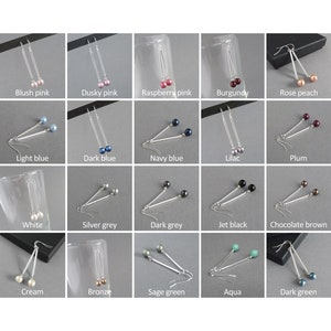 May include: A set of 20 pairs of dangle earrings with silver bars and different colored pearl beads. The earrings are displayed on a gray background.