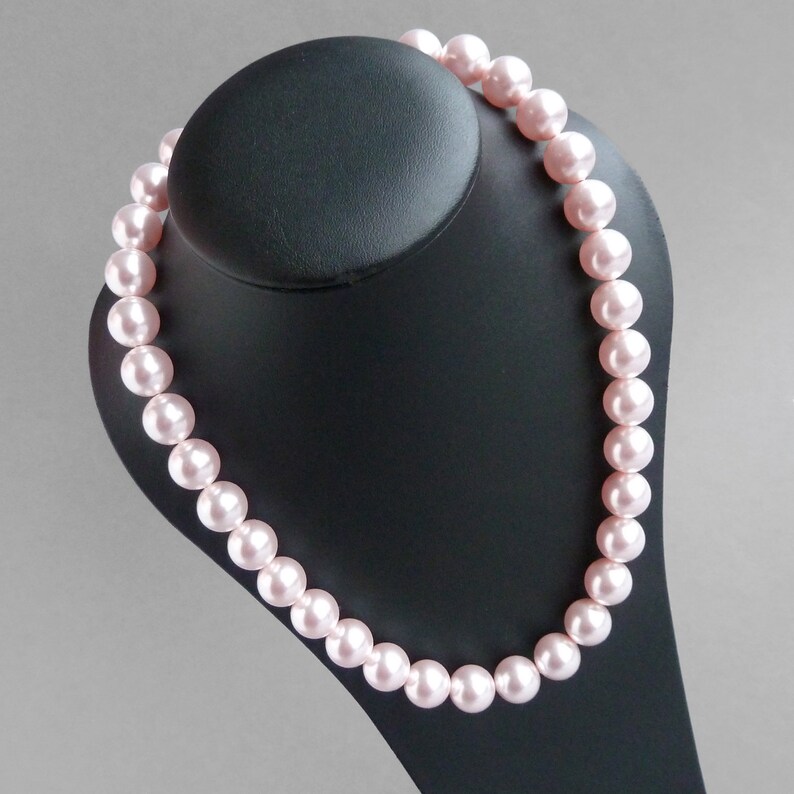 May include: A pink pearl necklace on a black display stand. The pearls are round and smooth.