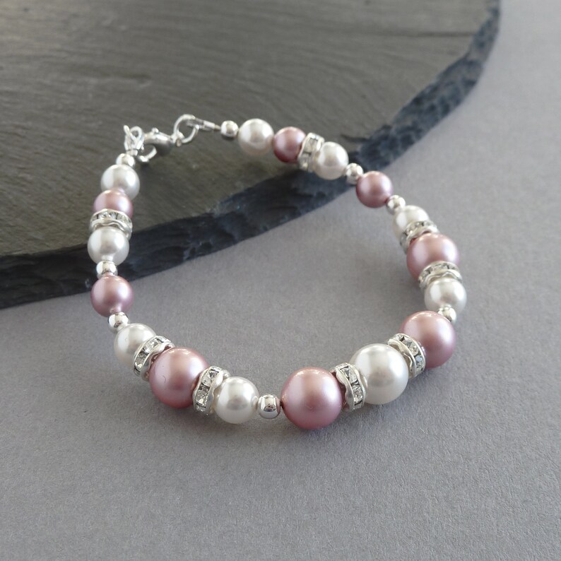 May include: A delicate bracelet featuring alternating pink and white faux pearls with clear rhinestone accents. The bracelet is made with a silver-toned clasp.