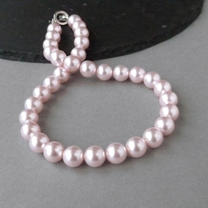 May include: A pink pearl necklace with a silver clasp. The pearls are round and smooth.