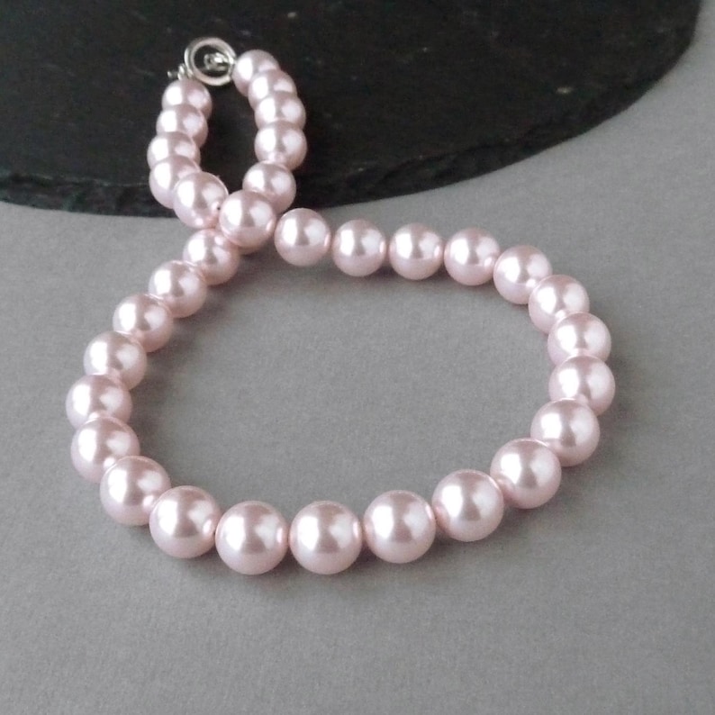 May include: A pink pearl necklace with a silver clasp. The pearls are round and smooth.