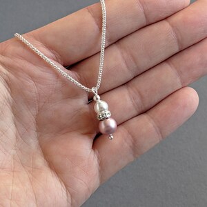 May include: A silver chain necklace with a pink and white pearl pendant. The pendant features a small silver bead with rhinestones.