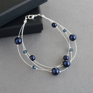 May include: A delicate bracelet featuring three strands of silver wire, embellished with dark blue pearls and small blue crystal accents.