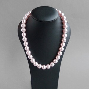 May include: A pink pearl necklace on a black display stand. The pearls are large and round.