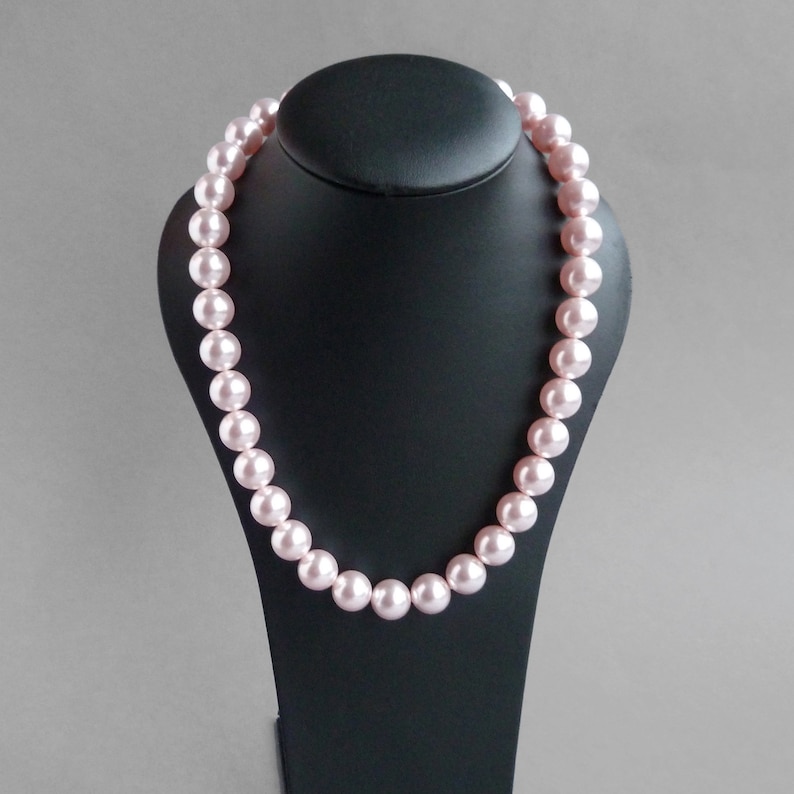May include: A pink pearl necklace on a black display stand. The pearls are large and round.