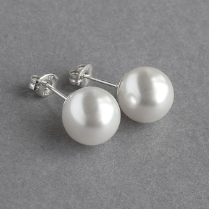 May include: A pair of silver stud earrings with white pearl accents.