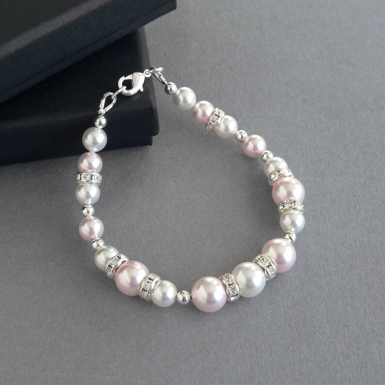 May include: A delicate bracelet featuring alternating pink and white pearls with rhinestone accents. The bracelet is made with a silver clasp.