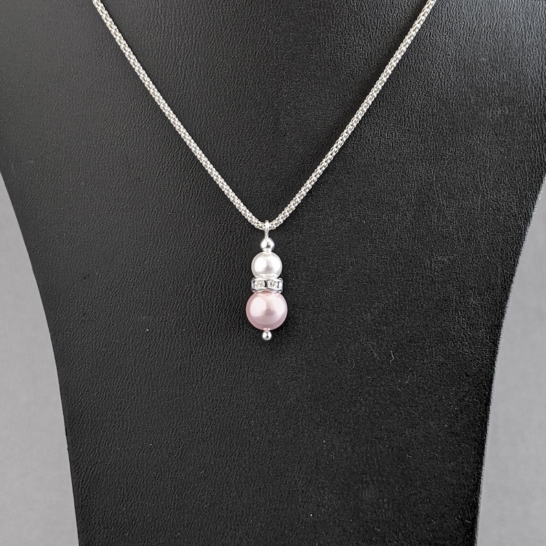 May include: A silver chain necklace with a pink and white pearl pendant. The pendant features a smaller white pearl on top of a larger pink pearl.
