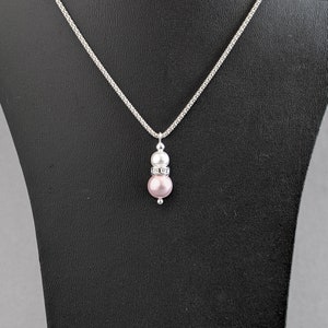 May include: A silver chain necklace with a pink and white pearl pendant. The pendant has a silver band with small clear stones.