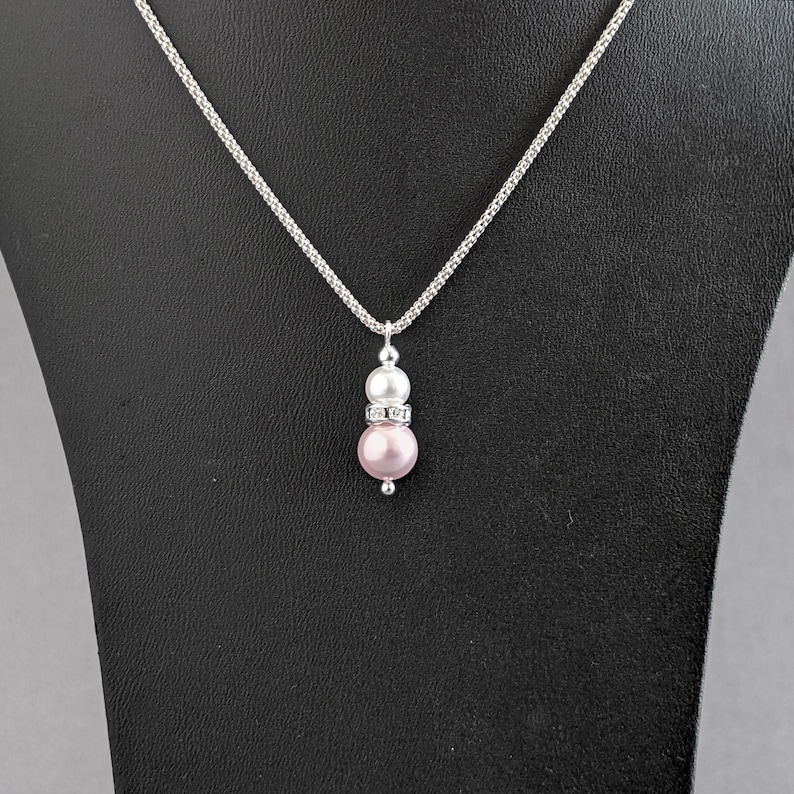 May include: A silver chain necklace with a pink and white pearl pendant. The pendant has a silver band with small clear stones.