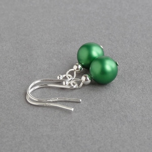 May include: A pair of silver dangle earrings with green round beads. The earrings have a simple design and are perfect for everyday wear.