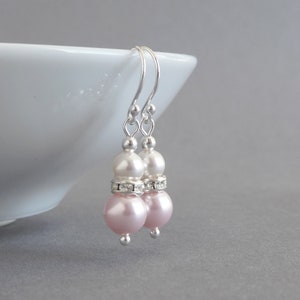 May include: A pair of silver dangle earrings with two pink and white pearls on each earring. The pearls are separated by a row of clear rhinestones.