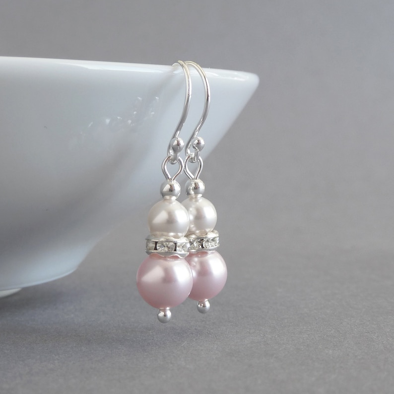 May include: A pair of silver dangle earrings with two pink and white pearls on each earring. The pearls are separated by a row of clear rhinestones.