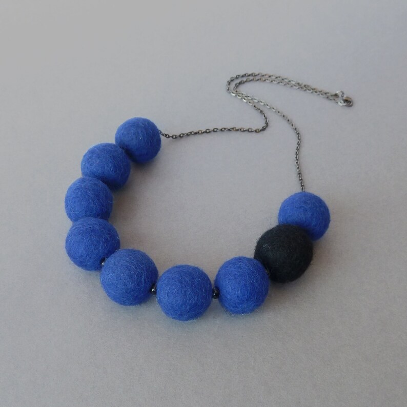 May include: A necklace with a silver chain and blue felt balls. One of the balls is black.