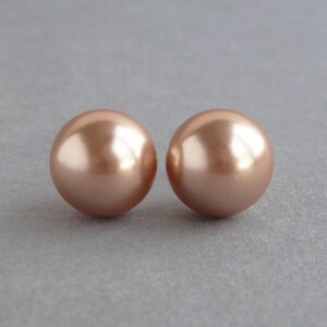 May include: A pair of rose gold pearl stud earrings. The pearls are round and have a smooth, shiny finish.