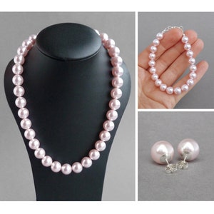 May include: A pink pearl necklace, bracelet, and earrings set. The necklace and bracelet are made of large, round pearls. The earrings are stud earrings with large, round pearls.