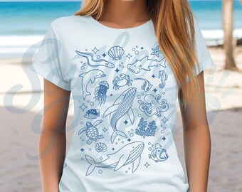 May include: White t-shirt featuring a blue line art design of various sea creatures, including a whale, octopus, and seahorse. The design also includes a crab, jellyfish, and other marine life. The shirt is a light blue color.