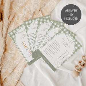 May include: A collection of baby shower game cards with a green gingham border. The cards feature various game titles and questions, with the text "Answer Key Included" on a circular label. The overall design is soft and neutral.