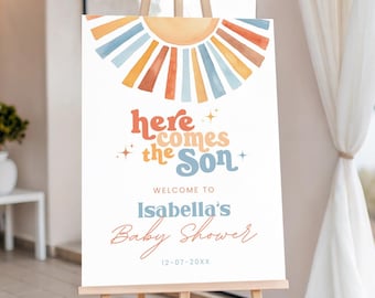 Könnte beinhalten: Willkommensschild für eine Babyparty auf einer Staffelei. Das weiße Schild zeigt ein Aquarell-Sonnendesign in Orange, Blau und Gelb. Der Text lautet "Here Comes the Son", "Welcome to Isabella's Baby Shower" und das Datum.