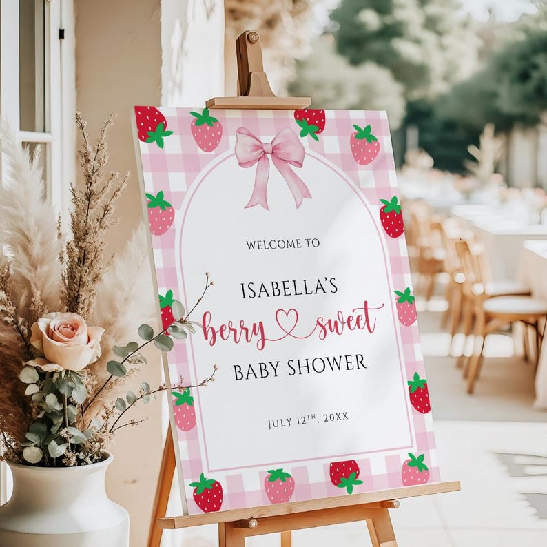May include: A pink and white gingham baby shower welcome sign with strawberry illustrations and a pink bow. The sign reads "Welcome to Isabella's berry sweet baby shower" and includes the date July 12th, 20XX.