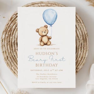 May include: A light beige birthday invitation featuring a watercolor illustration of a teddy bear holding a blue balloon. The invitation text reads "Join us to celebrate Hudson's Beary First Birthday" with event details.