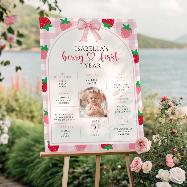 May include: A pink and white strawberry-themed first year milestone sign for a baby named Isabella. The sign includes a photo, nicknames, measurements (22 lbs, 29 in), favorite things, and the text "berry first year".