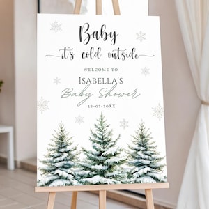May include: A white sign on an easel with the text "Baby it's cold outside" and "Welcome to Isabella's Baby Shower". The sign features snowflakes and snowy evergreen trees at the bottom. The date 12-07-20XX is also included.