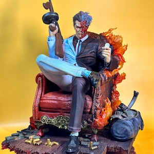 May include: A detailed statue of the DC Comics villain Two-Face, seated in a red armchair. He holds a Tommy gun and a coin, with one side of his face scarred. The base features bullets and a duffel bag, with flames around the chair.