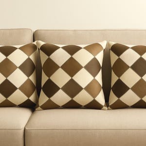 Könnte beinhalten: Drei braune und weiße Kissen mit Muster auf einem beigen Sofa.