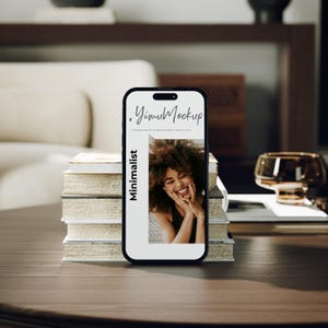 May include: A black smartphone with a screen showing a smiling woman. The screen displays the text "YimuMockup" and "Minimalist". The phone is placed on a stack of books on a dark wooden table.