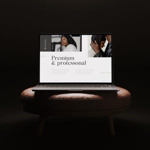 May include: A laptop displaying a webpage with the text "Premium & professional" is placed on a brown leather ottoman with wooden legs. The screen shows two images of people. The background is dark.