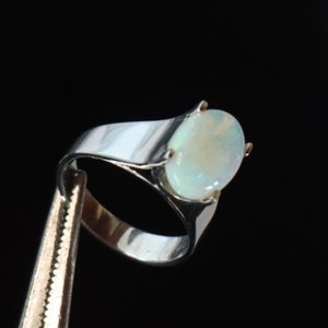 Könnte beinhalten: Ein silberner Ring mit einem weißen Opal-Edelstein. Der Ring hat eine schlichte Band und eine Krappenfassung für den ovalen Stein.