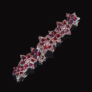 以下が含まれることがあります： 赤いガーネットの花の形をしたチャームが連なったシルバーブレスレット。ブレスレットはシルバー製で、繊細なチェーンが付いています。
