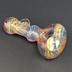 May include: A colorful glass pipe with a rounded bowl and a curved stem. The pipe features a blend of yellow, blue, and orange hues, with a textured, patterned design. The pipe is designed for smoking.