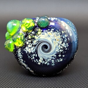 May include: A blue glass pipe with a swirling white and gold design. The pipe has a small opening on the side and is decorated with green and yellow glass beads.